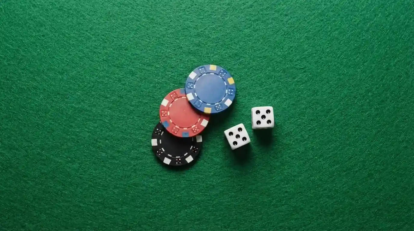 Vista cenital de fichas de casino y dados sobre una mesa de fieltro verde bajo luz suave.